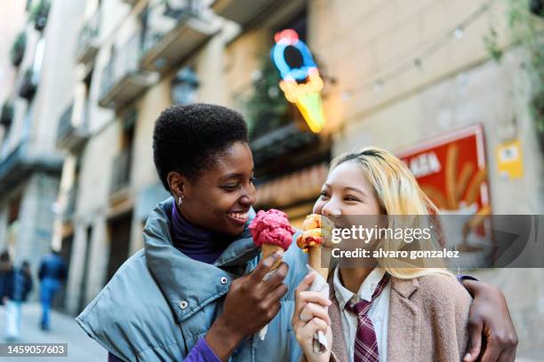 multiethnic lesbian couple eating an ice-cream together in the street - lesbian stockfoto's en -beelden