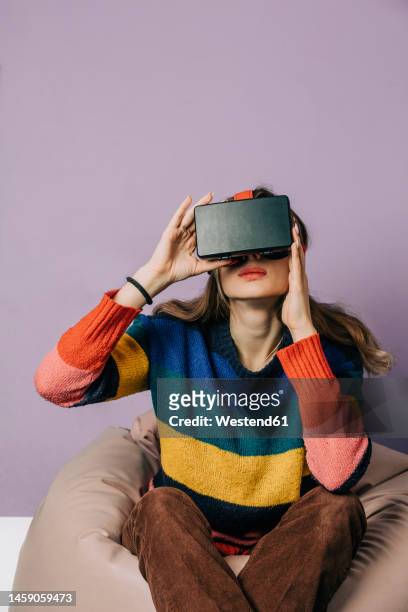 girl wearing visual reality simulator sitting on bean bag against purple background - top prospects game stockfoto's en -beelden