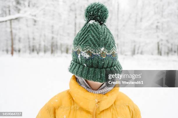 boy covering face with green knit hat at winter park - knit hat stock pictures, royalty-free photos & images