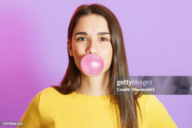 young woman blowing bubble gum against purple background - kauwgom stockfoto's en -beelden