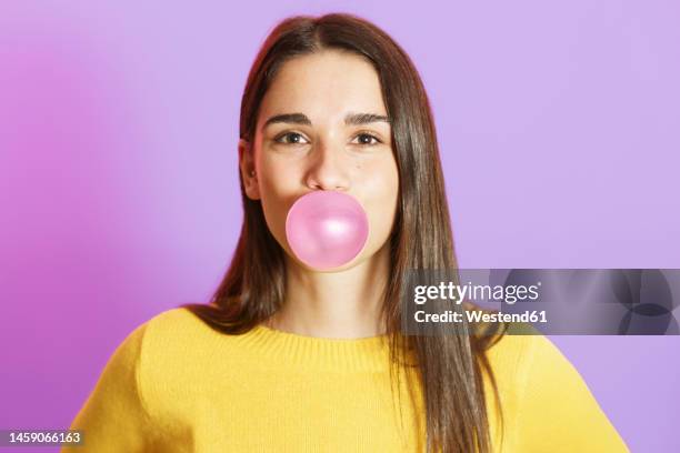 young woman blowing bubble gum against purple background - chewing gum stock pictures, royalty-free photos & images