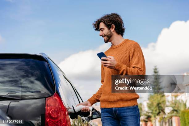 smiling young man charging car at vehicle charging station - plugging in stock pictures, royalty-free photos & images