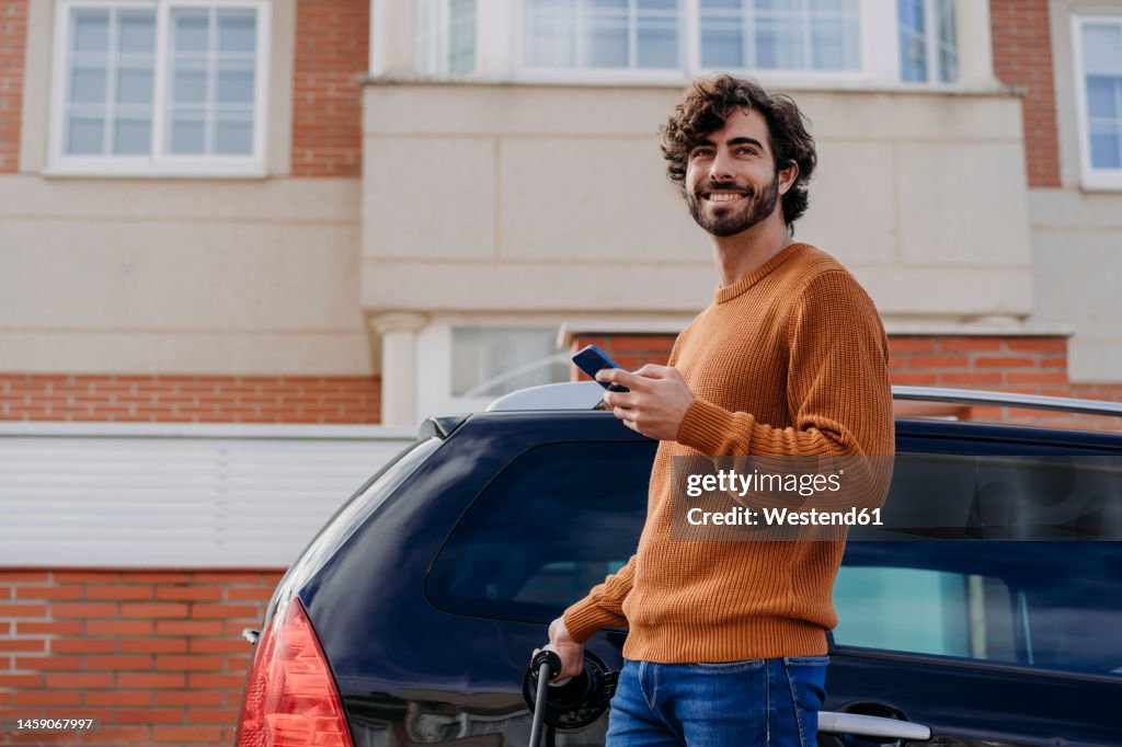 Happy young man charging car in front of building