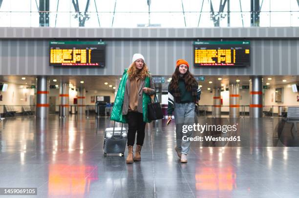woman and daughter with suitcase walking at train station - departure board front on fotografías e imágenes de stock