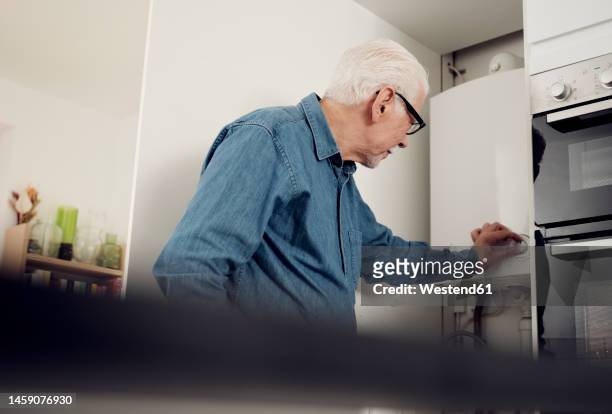 senior man adjusting boiler for energy saving at home - caldaia foto e immagini stock