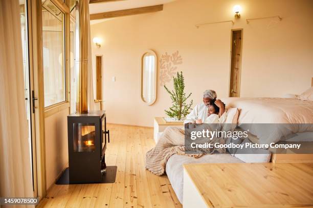 couple in bathrobes relaxing over coffee in front of a fireplace during vacation - log cabin fire stock pictures, royalty-free photos & images