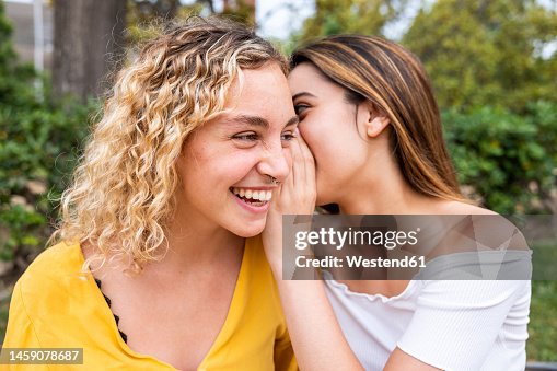 Young woman whispering into friend's ear in park Young woman whispering into friend's ear in park