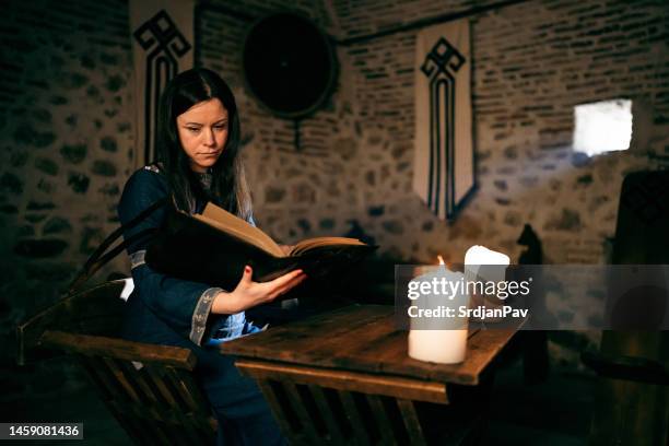 mujer medieval sentada junto al escritorio y leyendo un libro con la ayuda de la luz de las velas - caballerosidad fotografías e imágenes de stock