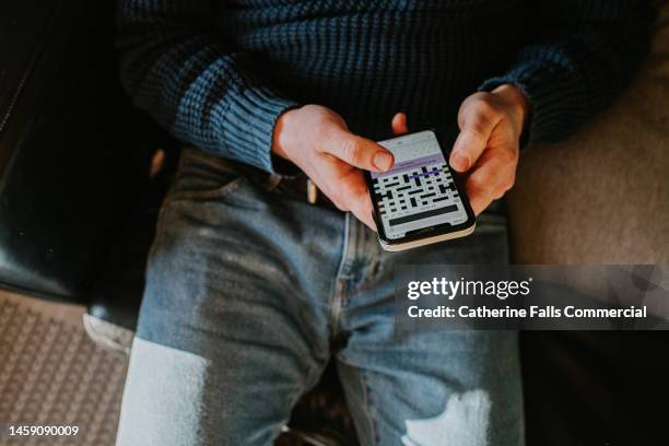 close-up of a man attempting to solve a cryptic crossword on a phone app - kruiswoordpuzzel stockfoto's en -beelden