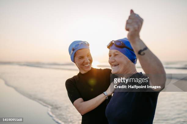 daughter with her elder mother in neoprene enjoying time at ocean. - senior swimming stock pictures, royalty-free photos & images