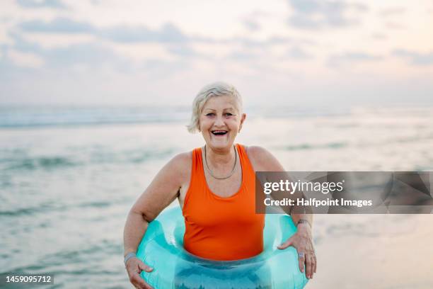 happy senior woman with inflatable wheel on the beach. - old woman in swimsuit stock pictures, royalty-free photos & images
