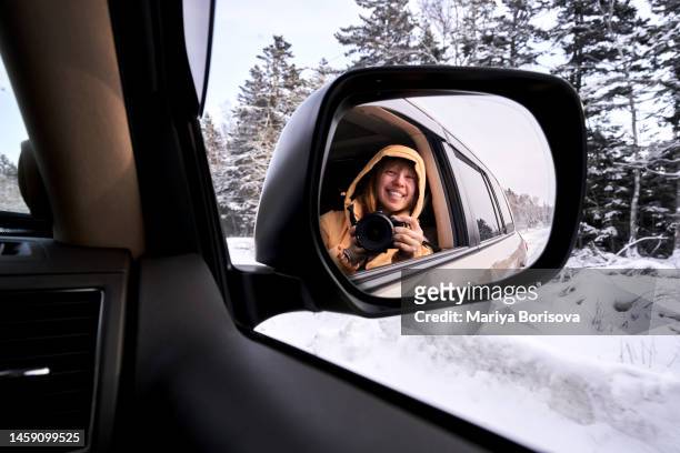 a woman in a yellow jacket takes a picture of herself in the rearview mirror of a car. - auto von hinten winter stock-fotos und bilder