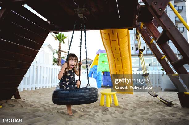 little girl at a beach sandy playground. - tire swing stock pictures, royalty-free photos & images