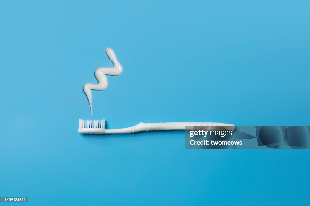Flat lay white toothbrush and tooth paste on blue background.
