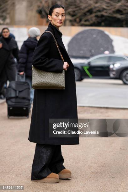 Guest wears a black coat, Ugg shoes and Louis Vuitton bag, outside Schiaparelli, during Paris Fashion Week - Menswear Fall-Winter 2023-2024, on...