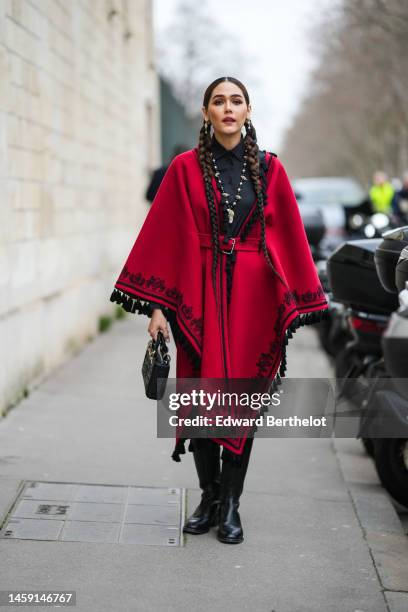 Araya Hargate wears gold and pearls earrings, a black t-shirt, a black and white pearls necklace, a red with embroidered black borders pattern wool...