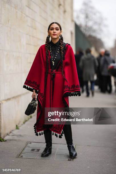 Araya Hargate wears gold and pearls earrings, a black t-shirt, a black and white pearls necklace, a red with embroidered black borders pattern wool...