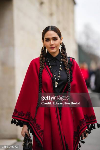 Araya Hargate wears gold and pearls earrings, a black t-shirt, a black and white pearls necklace, a red with embroidered black borders pattern wool...
