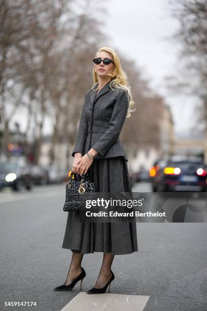 Sabine Getty wears black sunglasses, a dark gray buttoned blazer jacket, a matching dark gray pleated midi skirt, a dark gray and black leopard print...