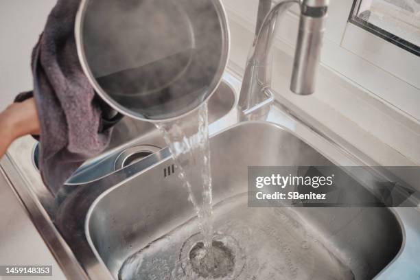 pouring boiling water to unclog the kitchen sink - bollente foto e immagini stock