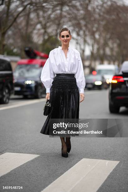Chiara Ferragni wears gold earrings, a white pleated shirt, a black shiny leather pleated / accordion midi skirt from Dior, a black shiny leather...