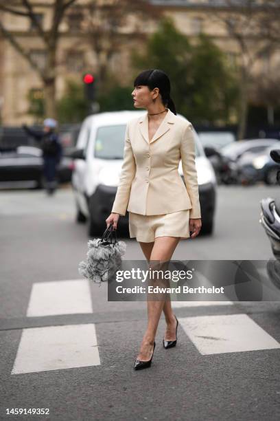 Akimoto Kozue wears black earrings, a black leather necklace, a white latte buttoned blazer jacket, white latte suit shorts, a white and black print...