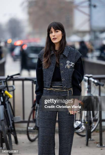 Leia Sfez wears striped black white vest, wide leg pants, golden belt, bag with black white helmet shape, black jumper outside Chanel during Paris...