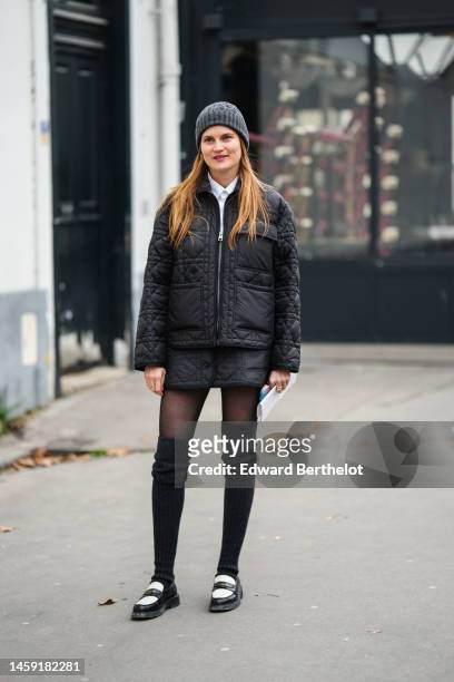 Eugenie Trochu wears a gray wool beanie, a white shirt, a black quilted zipper jacket from Dior, a matching black quilted short skirt, black tights,...