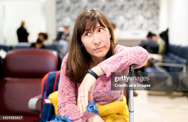 caucasian woman, long brown hair, happy looking at the camera, with her suitcase in the airport waiting room - transfer image stock pictures, royalty-free photos & images