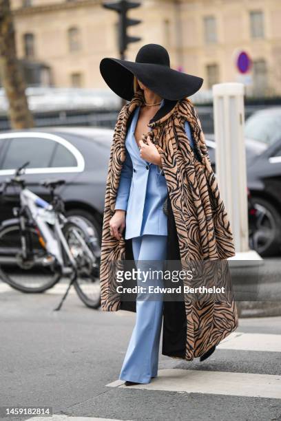 Guest wears a black oversized felt / wool hat, a white pearls necklace, a pale blue blazer jacket, matching pale blue flared pants, a brown and black...