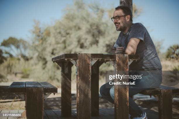 smiling man sitting on a picnic bench under a pergola, albufera, valencia, spain - shade45 stock pictures, royalty-free photos & images