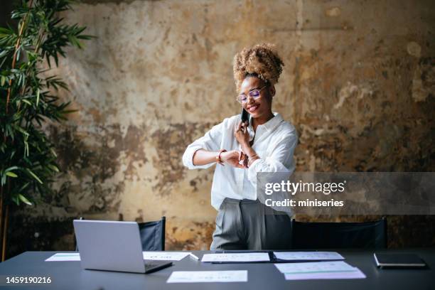 happy businesswoman talking on a mobile phone and looking at wristwatch in the office - business woman working late stock pictures, royalty-free photos & images