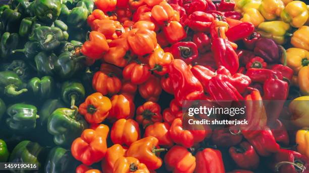 full frame close-up of red, orange, yellow and green bell peppers at a market - gele paprika stockfoto's en -beelden