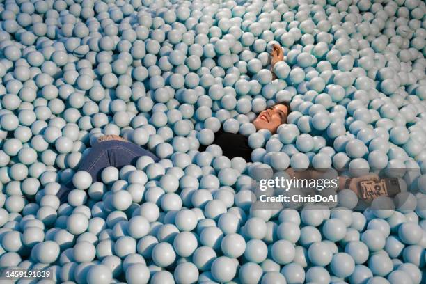 happy woman playing in a ball pool filled with plastic blue balls - ball pit stock pictures, royalty-free photos & images