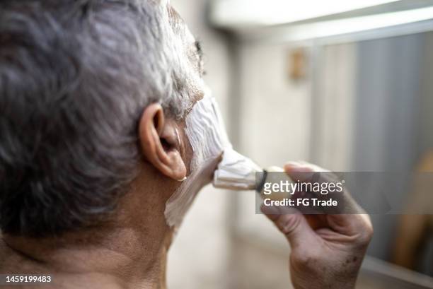 nahaufnahme eines älteren mannes, der rasierschaum auf das gesicht vor dem spiegel im badezimmer zu hause reicht - shaving brush stock-fotos und bilder