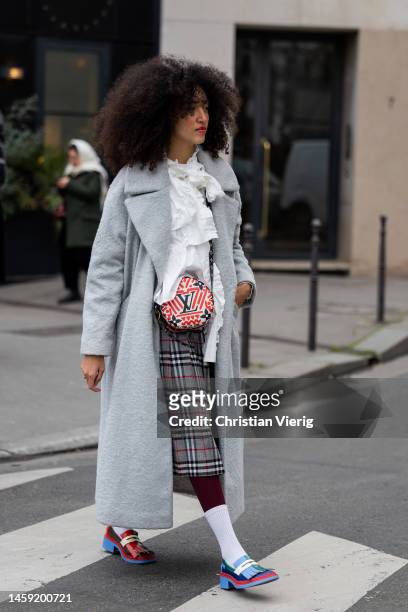 Guest wears round Louis Vuitton bag, grey coat, ruffled blouse, grey checkered skirt, white socks, loafers outside Alexis Mabille during Paris...