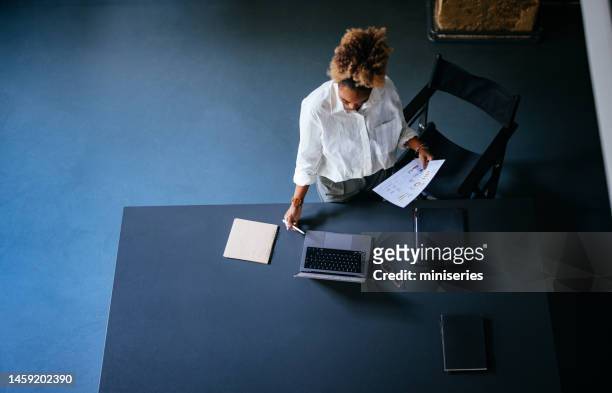 high angle view of unrecognizable woman reading business report on a laptop computer and documents in the cafe - high tech beauty stockfoto's en -beelden
