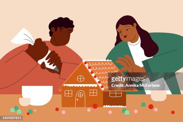 a multiracial couple decorates a gingerbread house together for christmas - gingerbread house stock illustrations
