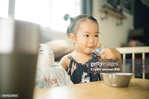 candid asian baby girl enjoys eating and playing at living room domestic life - asian baby eating stock pictures, royalty-free photos & images