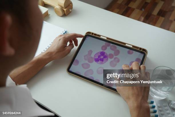 asiatische männer, die eine blutleukämiezellen per digitalem tablet suchen, um das stadium ihrer eigenen leukämie zu kennen. - platelet stock-fotos und bilder