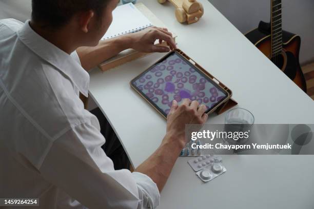 asian men looking a blood leukemia cells by digital tablet to know the stage of your own leukemia. - anemia stock pictures, royalty-free photos & images
