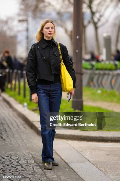 Guest wears a black high neck pullover, a black bomber coat, navy blue denim pants, a yellow shiny leather Chanel 22 shoulder bag from Chanel, black...