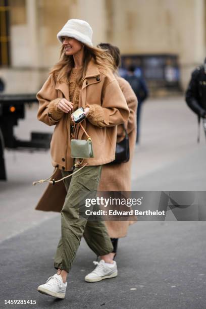 Guest wears a white fluffy bob, a beige wool jacket, a brown embroidered logo pullover from Loewe, a khaki embossed LV monogram pattern handbag from...