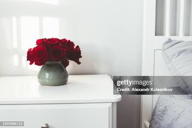 red roses in vase on white bedside table by wall at home - nachttisch stock-fotos und bilder
