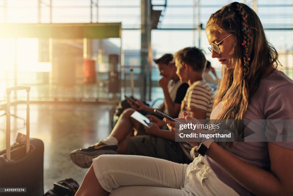 Teenagers waiting at the airport and playing with smart devices