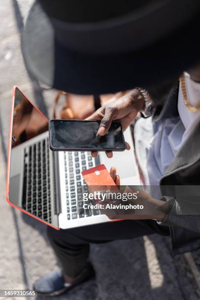 unrecognizable black man shopping online with bank card on computer while validating with mobile phone - agarrar stock pictures, royalty-free photos & images