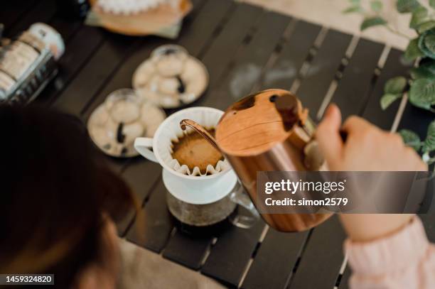 eine asiatische frau, die heißes wasser aus dem wasserkocher gießt, um auf dem campingplatz tropfkaffee zuzubereiten - filterkaffee stock-fotos und bilder