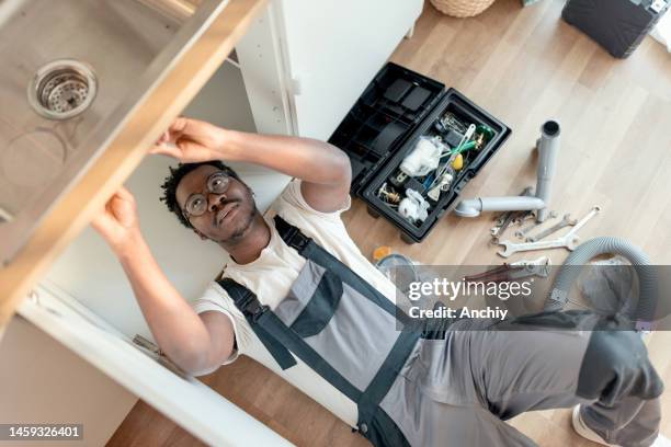 plumber working on pipes under sink - loodgieter stockfoto's en -beelden