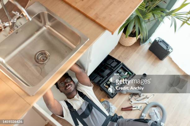 plumber working on pipes under sink - gootsteen stockfoto's en -beelden