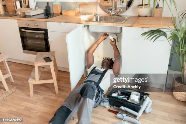 plumber working on pipes under sink - gootsteen stockfoto's en -beelden